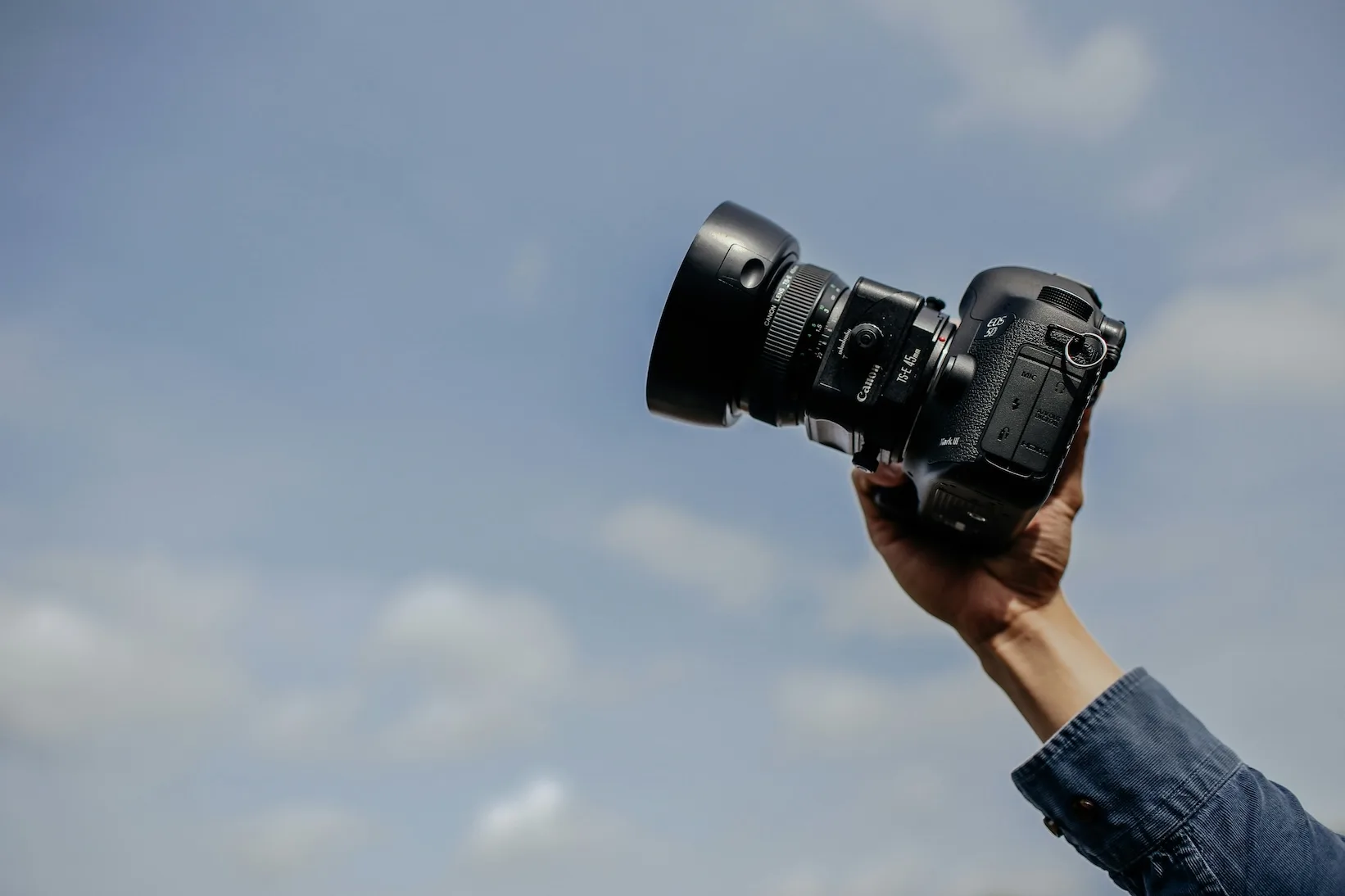 Hand holding a Canon camera against a blue sky
